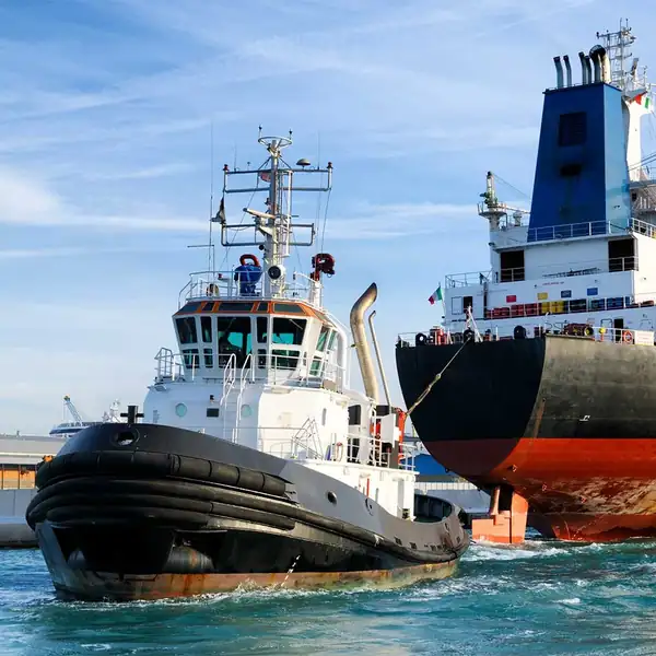 Harbour tug working alongside the bow of a cargo ship.